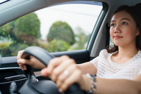 Happy Asian woman driving the electric vehicle - EV car smiling and showing her thumb up to the...