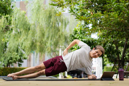 Active sportsman doing a side plank exercise and making a video call with a friend and online sport...