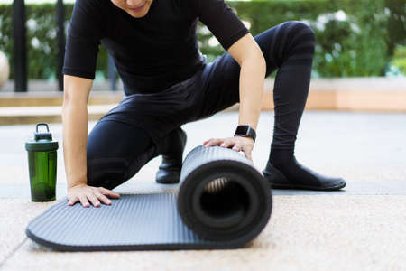 Active Asian sportsman unroll an exercise mat on the floor, healthy and fit body of Asian sport man preparing a workout yoga mat for body weight and cardio exercise.の写真素材