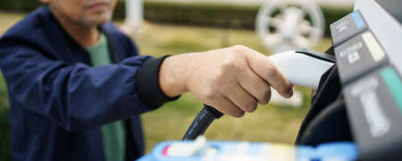 Asian man preparing to charge his electric car or EV at charging station, man holding a Type 2 BEV...