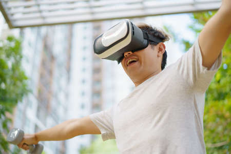 Active Asian sportsman doing a weight training exercise by using dumbbell and virtual reality - VR...