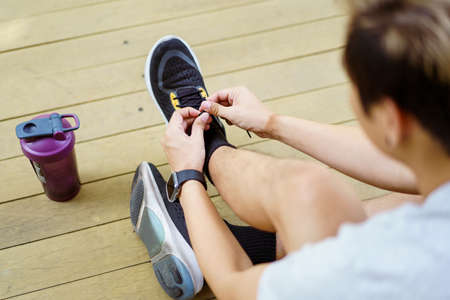 Happy Asian young sportsman trying to tie shoelaces before getting an exercise, man preparing for out workout. Healthy Asian young sporty man tie up a running shoes before running.の写真素材