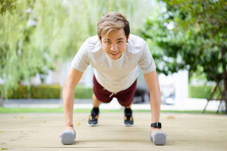 Active Asian sportsman making a body weight exercise, man doing push up workout with dumbbell. Intensive bodybuilding workout training.の写真素材