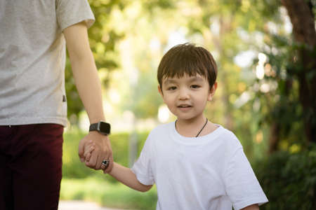 Happy Asian little boy enjoy playing and walking at the park with daddy close up, Asian boy have a beautiful smiling while looking at his father. Little boy portrait at the park and playground.の写真素材
