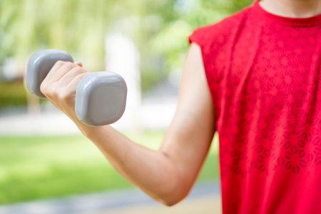 Active Asian young man doing a weightlifting by using dumbbell, beginner muscular bodybuilder man in red shirt lift up a dumbell.の写真素材