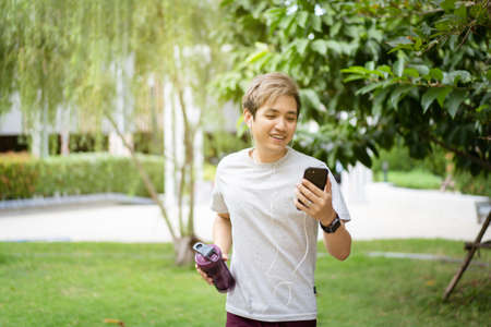 Handsome Asian young sportsman posing and smiling to the camera while his running exercise, man listening a music on smartphone while practicing running workout. Happy Asian athlete smiling.の写真素材