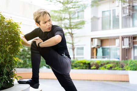 Happy Asian young sportsman doing a lower and upper body stretching before making an exercise in a park, stretching and workout concept. Sport man making a cardio and weight training workout.の写真素材