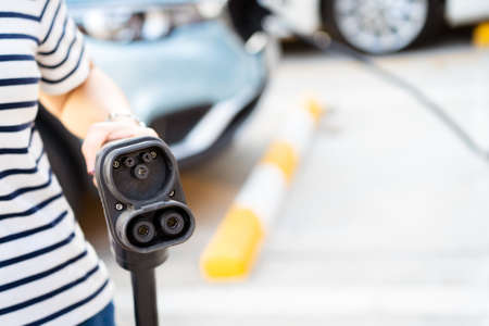 Unrecognizable Asian woman holding aa DC - CCS type 2 EV charging connector at EV charging station, woman preparing an EV - electric vehicle charging connector for recharge a vehicle.の写真素材