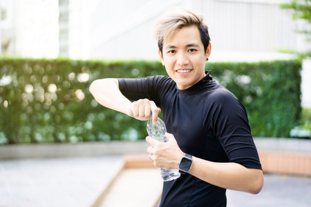 Active Asian sportsman relaxing and drinking a water in bottle after outdoor running or workout. Asian man drink a water during the break from exercise. A healthy man trying hard for cardio workout.の写真素材