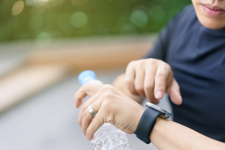 Active Asian young sportsman using a smartwatch or smart fitness band to track his outdoor workout and activities, man reviewing an exercise and health information after finished outdoor workout.の写真素材