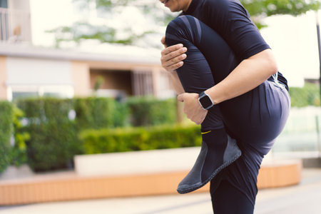 Happy Asian young sportsman doing a lower and upper body stretching before making an exercise in a park, stretching and workout concept. Sport man making a cardio and weight training workout.の写真素材