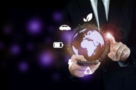 Unrecognizable smart businessman in casual business suit holding a smartphone and pointing with graphic in Electric Vehicle or EV innovation concept. Internet of things era and globalization.の写真素材