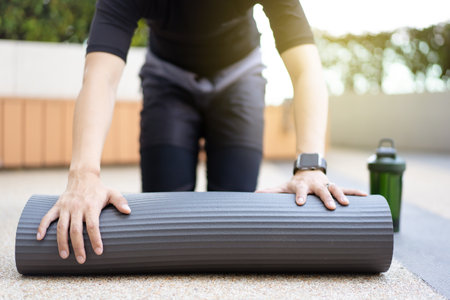 Active Asian sportsman unroll an exercise mat on the floor, healthy and fit body of Asian sport man preparing a workout yoga mat for body weight and cardio exercise.の写真素材