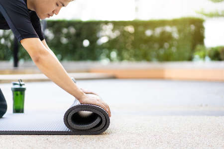 Active Asian sportsman unroll an exercise mat on the floor, healthy and fit body of Asian sport man preparing a workout yoga mat for body weight and cardio exercise.の写真素材