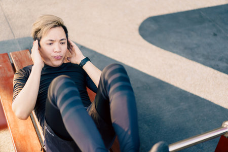 Active Asian young man doing a body weight exercise, man sit-up at the outdoor park. Healthy Asian man trying to sit-up to make a strong and good body muscle.の写真素材