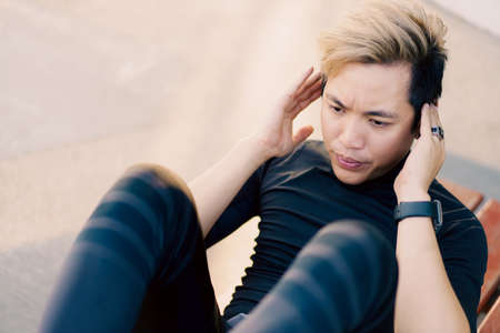 Active Asian young man doing a body weight exercise, man sit-up at the outdoor park. Healthy Asian man trying to sit-up to make a strong and good body muscle.の写真素材