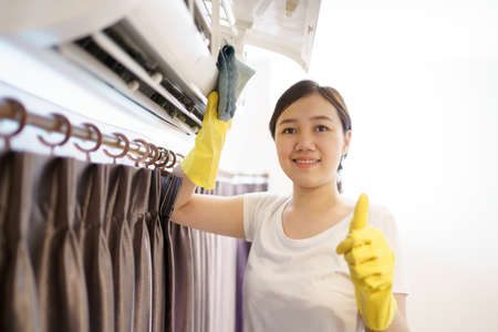 Asian woman cleaning a dirty and dusty air conditioning filter in her house. Housewife removing a dusty air conditioner filter.の写真素材