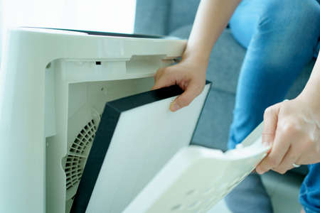 Asian young woman changing - fixing a dirty air purifier HEPA filter after using for a long time. A repairman replacing and installing the air purifier filter. Healthcare and wellbeing.の写真素材