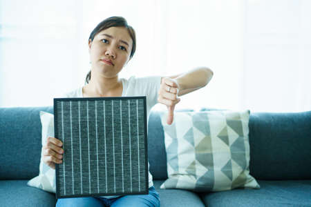 Young woman showing the used dirty air purifier filter to camera. HEPA filter used in high efficiency air purifier system to purify the dirty or polluted air inside the house or vehicle.の写真素材