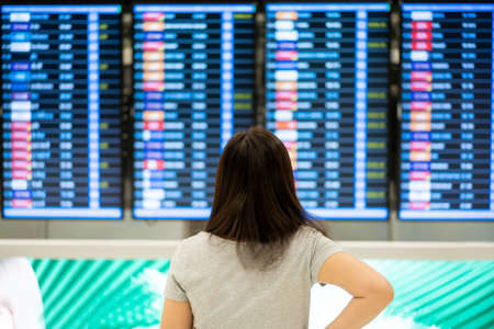 Beautiful Asian young woman with protective face mask standing in the airport and looking at the flight information. Woman wearing a face mask while traveling the coronavirus - COVID-19 pandemic.の写真素材