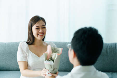 Happy Asian young couple in Valentine or anniversary stay together, man giving and surprise his wife a bouquet in their Valentine or Anniversary day. Husband and wife celebrating in Valentine day.の写真素材