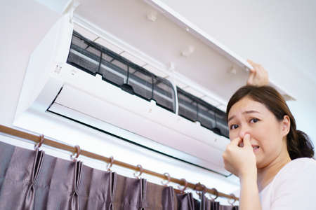 Asian woman cleaning a dirty and dusty air conditioning filter in her house. Housewife removing a dusty air conditioner filter.の写真素材