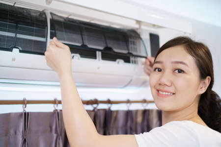 Asian woman cleaning a dirty and dusty air conditioning filter in her house. Housewife removing a dusty air conditioner filter.の写真素材