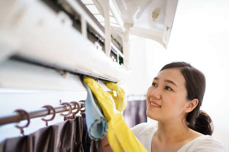 Asian woman cleaning a dirty and dusty air conditioning filter in her house. Housewife removing a dusty air conditioner filter.の写真素材