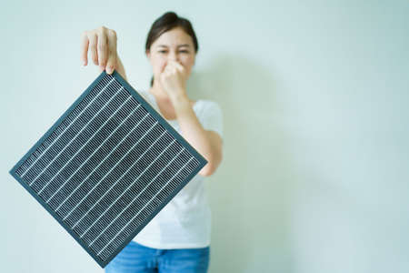 Young woman showing the used dirty air purifier filter to camera. HEPA filter used in high efficiency air purifier system to purify the dirty or polluted air inside the house or vehicle.の写真素材