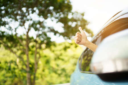Unrecognizable Asian woman driver showing a thumb up outside the vehicle while driving a car. Happy woman driver or passenger showing her thumb up during in the car. Safety trip and freedom concept.の写真素材