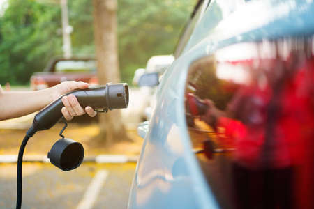 Unrecognizable Asian woman holding AC type 2 EV charging connector at EV charging station, woman preparing an EV - electric vehicle charging connector for recharge a vehicle.の写真素材
