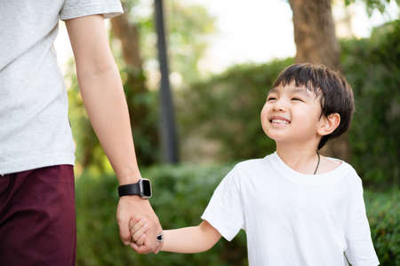 Happy Asian little boy enjoy playing and walking at the park with daddy close up, Asian boy have a beautiful smiling while looking at his father. Little boy portrait at the park and playground.の写真素材