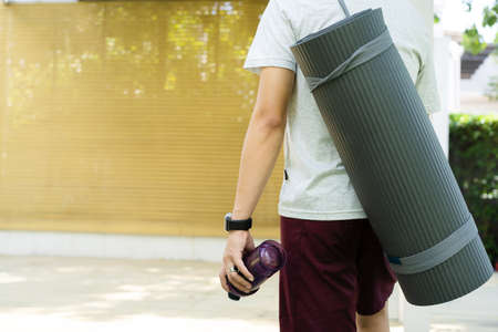 Active Asian sportsman preparing - unrolling an exercise or Yoga mat, healthy and fit body of Asian sport man preparing a workout yoga mat for body weight and cardio exercise.の写真素材