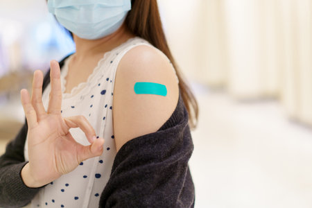 Happy Asian young woman wearing a protective face mask showing her vaccination spot on her arm, woman got a COVID-19 vaccine. Coronavirus or COVID-19 pandemic concept.の写真素材