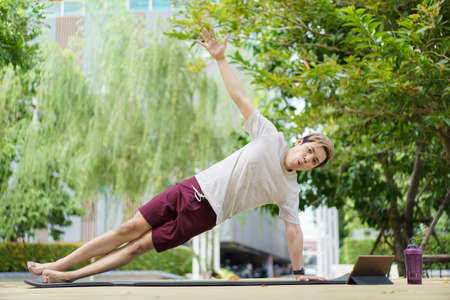 Active sportsman doing a side plank exercise and making a video call with a friend and online sport training coach. Healthy sport man making a body building workout with online instructor.の写真素材