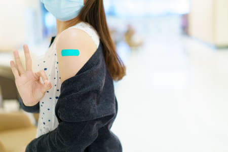 Happy Asian young woman wearing a protective face mask showing her vaccination spot on her arm, woman got a COVID-19 vaccine. Coronavirus or COVID-19 pandemic concept.の写真素材