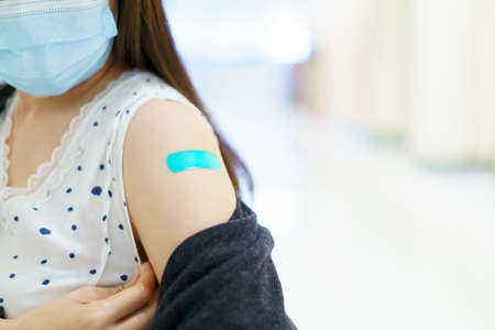 Happy Asian young woman wearing a protective face mask showing her vaccination spot on her arm, woman got a COVID-19 vaccine. Coronavirus or COVID-19 pandemic concept.の写真素材