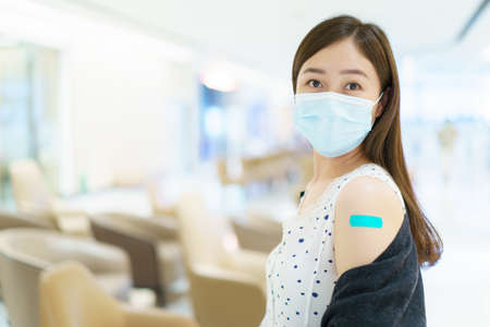 Happy Asian young woman wearing a protective face mask showing her vaccination spot on her arm, woman got a COVID-19 vaccine. Coronavirus or COVID-19 pandemic concept.の写真素材