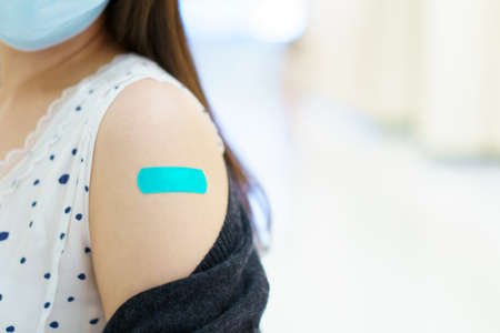 Happy Asian young woman wearing a protective face mask showing her vaccination spot on her arm, woman got a COVID-19 vaccine. Coronavirus or COVID-19 pandemic concept.の写真素材