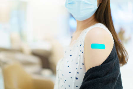 Happy Asian young woman wearing a protective face mask showing her vaccination spot on her arm, woman got a COVID-19 vaccine. Coronavirus or COVID-19 pandemic concept.の写真素材