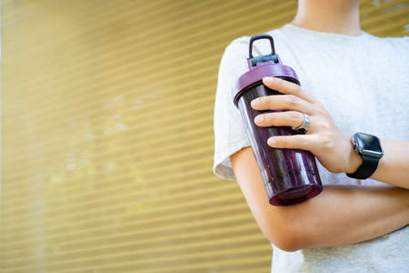 Active Asian sportsman relaxing and drinking a water in bottle after outdoor running or workout. Asian man drink a water during the break from exercise. A healthy man trying hard for cardio workout.の写真素材