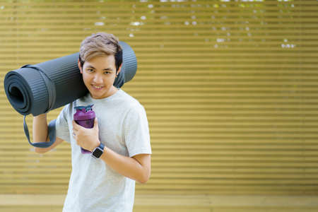 Active Asian sportsman preparing - unrolling an exercise or Yoga mat, healthy and fit body of Asian sport man preparing a workout yoga mat for body weight and cardio exercise.の写真素材