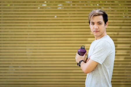 Active Asian sportsman relaxing and drinking a water in bottle after outdoor running or workout. Asian man drink a water during the break from exercise. A healthy man trying hard for cardio workout.の写真素材