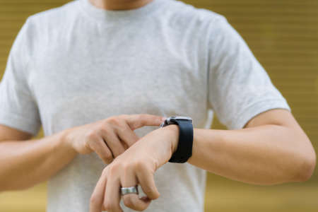 Active Asian young sportsman using a smartwatch or smart fitness band to track his outdoor workout and activities, man reviewing an exercise and health information after finished outdoor workout.の写真素材