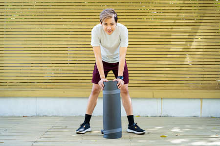 Active Asian sportsman preparing - unrolling an exercise or Yoga mat, healthy and fit body of Asian sport man preparing a workout yoga mat for body weight and cardio exercise.の写真素材