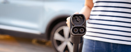Unrecognizable Asian woman holding aa DC - CCS type 2 EV charging connector at EV charging station, woman preparing an EV - electric vehicle charging connector for recharge a vehicle.の写真素材