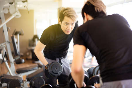 Active Asian sportsman doing a weight exercise in a gym - fitness by lifting up a dumbbell, man lifting up or holding a heavy dumbbell from dumbbell rack.の写真素材