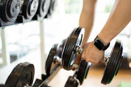 Active Asian sportsman doing a weight exercise in a gym - fitness by lifting up a dumbbell, man lifting up or holding a heavy dumbbell from dumbbell rack.の写真素材