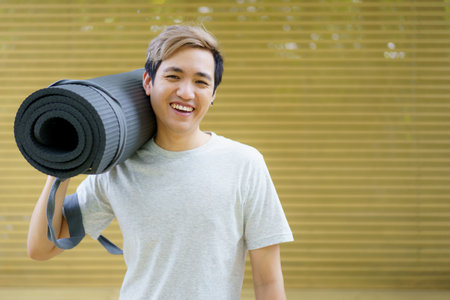 Active Asian sportsman preparing - unrolling an exercise or Yoga mat, healthy and fit body of Asian sport man preparing a workout yoga mat for body weight and cardio exercise.の写真素材