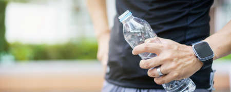 Active Asian sportsman relaxing and drinking a water in bottle after outdoor running or workout. Asian man drink a water during the break from exercise. A healthy man trying hard for cardio workout.の写真素材